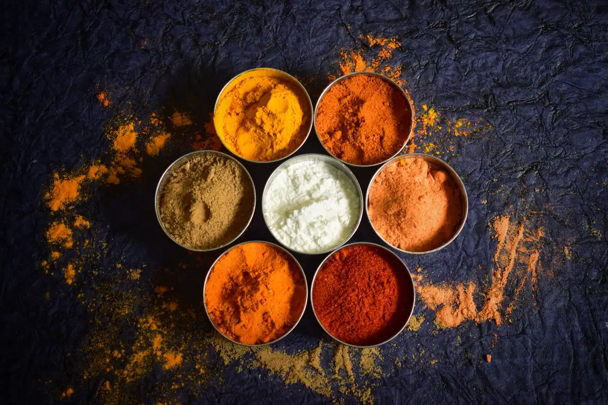 Boluri cu mirodenii colorate pe un fundal închis, ingrediente care colorează și aromatizează natural