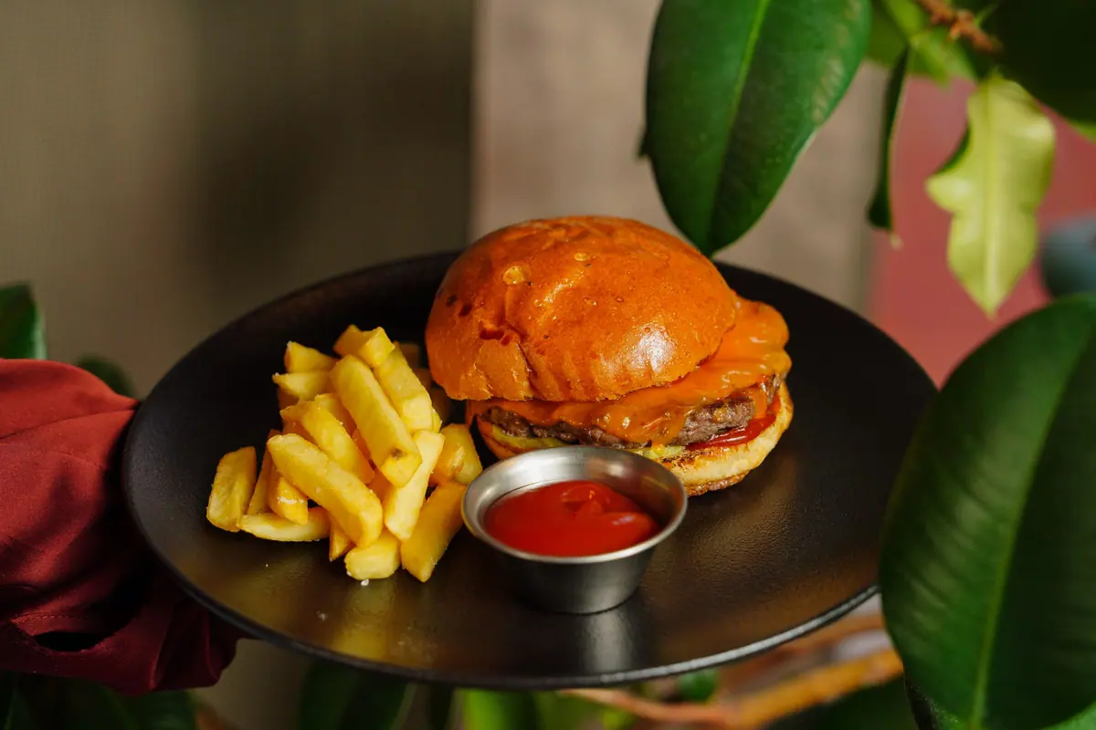 Burger cu cartofi prăjiți și ketchup pe o farfurie neagră, exemplu de preparat ultraprocesat