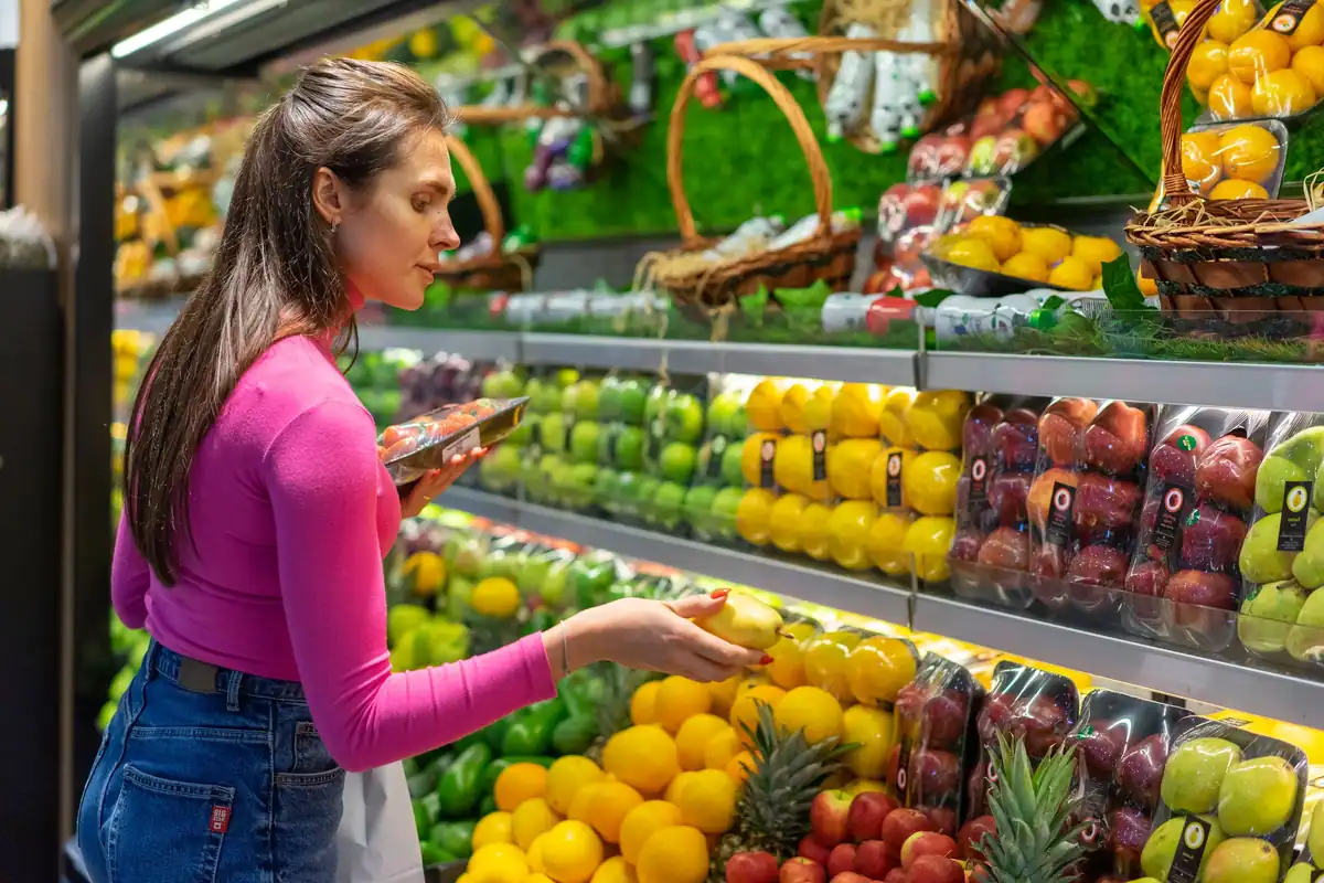 Femeie care alege fructe la raftul unui magazin, atentă la valorile nutriționale