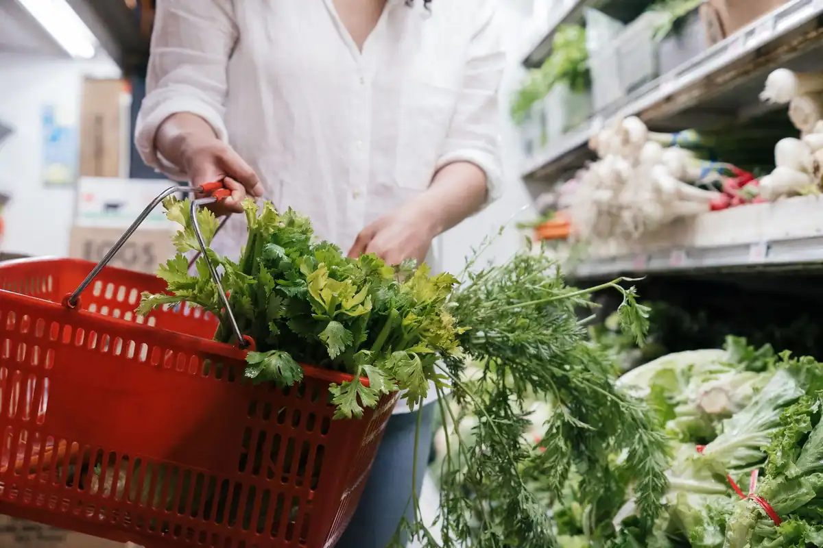 Persoană cu un coș plin cu verdeață proaspătă într-un magazin alimentar