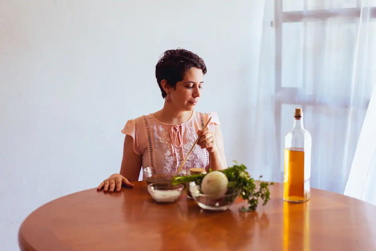 Femeie la masă care pregătește legume cu ulei, grăsime ce ajută absorbția vitaminelor